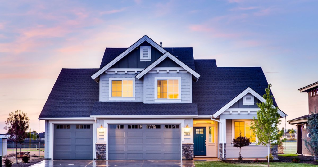 Two-story suburban home with a lit front porch and garage at dusk after rain